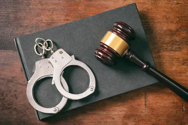 Handcuffs and a judge’s gavel on a textured black notebook atop a wooden surface